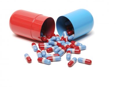 Big batch of red, white, and blue medicine pills spilling out of a bigger red and blue capsule canister on white background